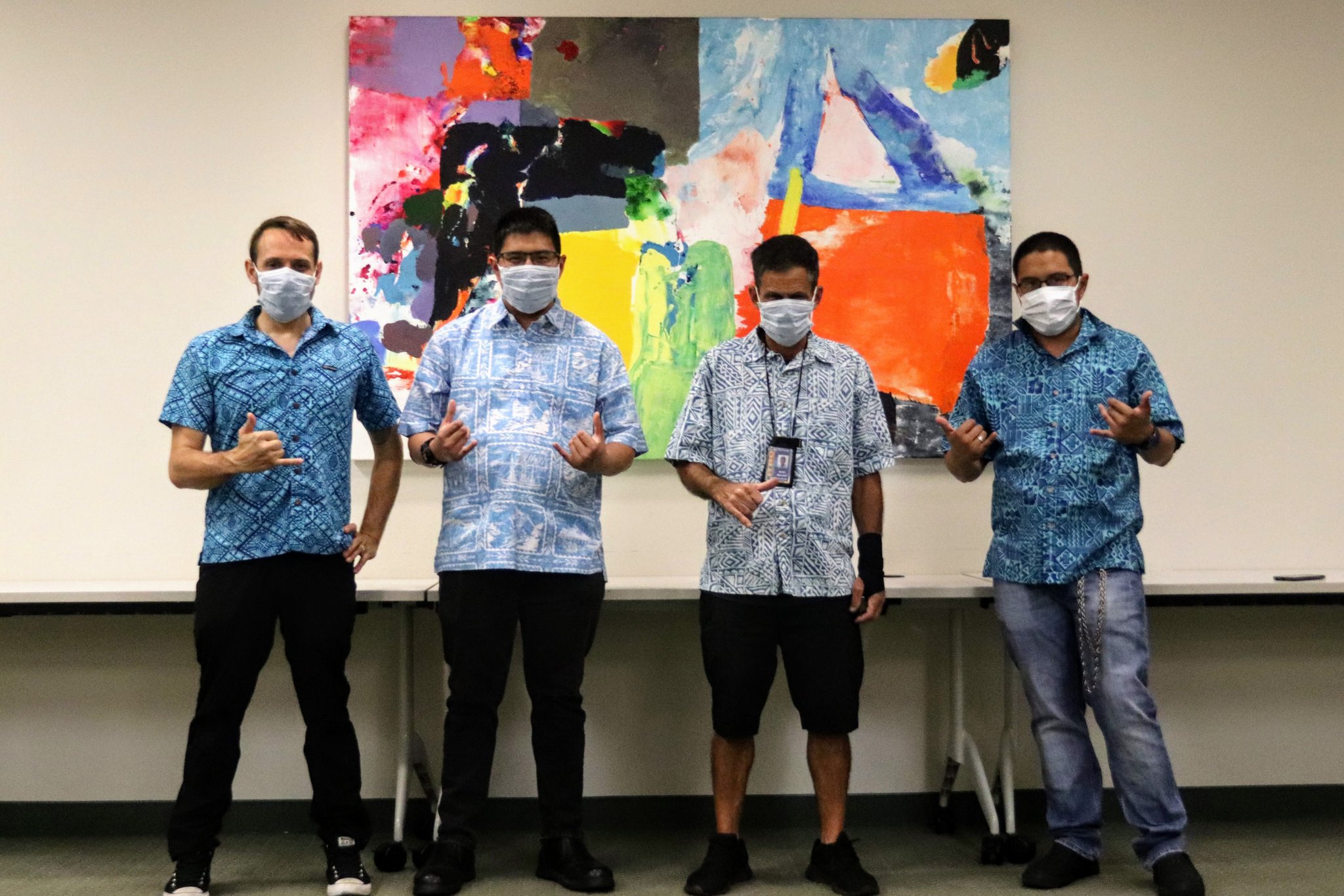 Four men standing in a row, wearing masks