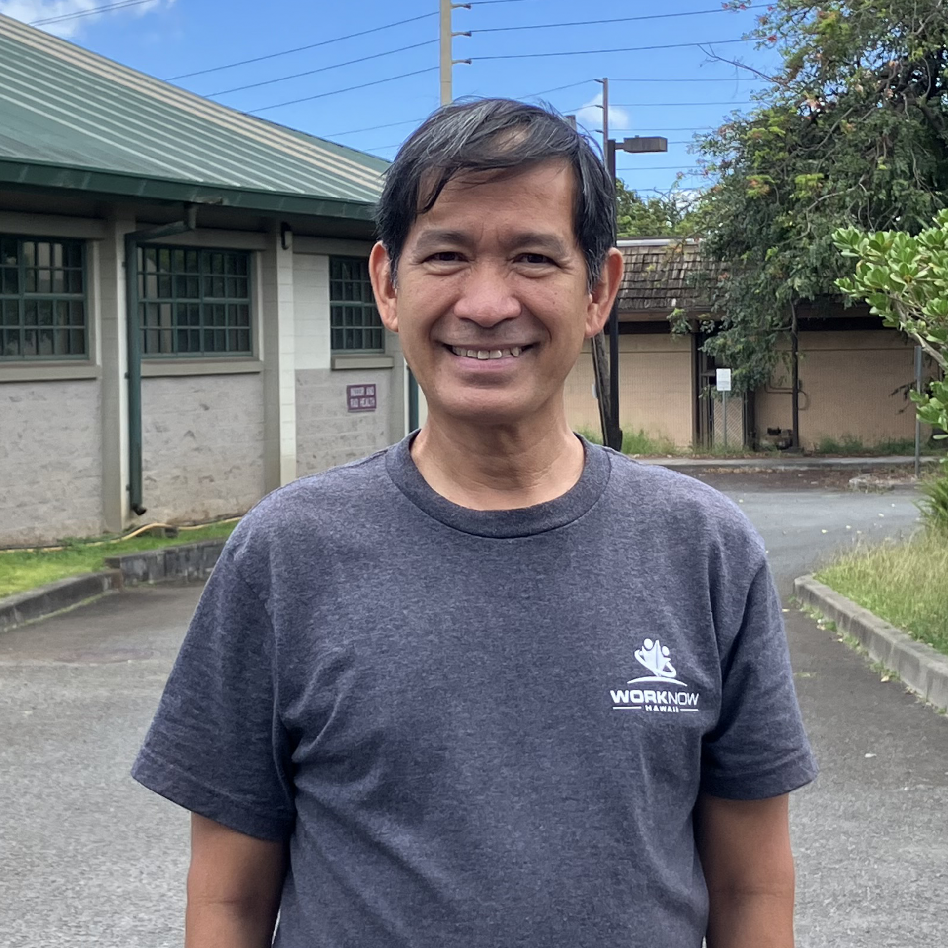 Image of Hernani standing outside a building, in his Work Now Hawaii shirt.