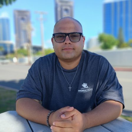 Image of smiling Isaiah, sitting at a table in his Work Now Hawaii shirt.
